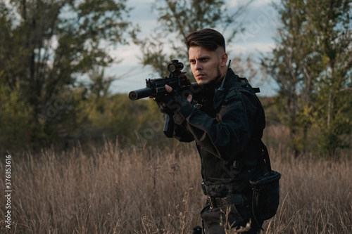 Young soldier in black uniform aiming an assault rifle. Copy space.