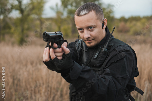 Special forces soldier in black uniform aiming a pistol.