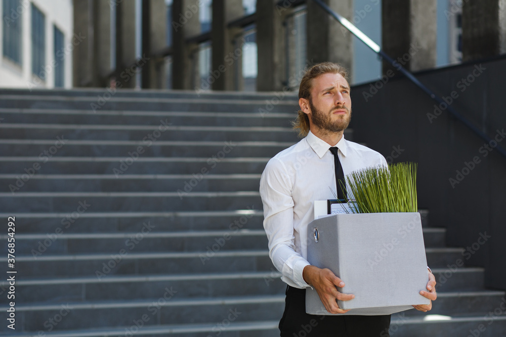 An unhappy young manager in a white shirt is fired from his job. A sad worker sits on the steps of a business center after layoffs. Crisis and unemployment. An unhappy young manager in a white shirt is fired from his job. A sad worker sits on the steps of a business center after layoffs. Crisis and unemployment.