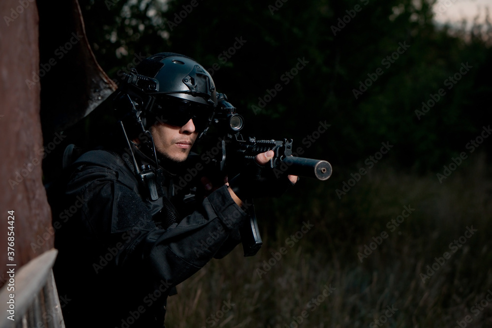 Special force soldier in black uniform helmet and glasses aiming an assault rifle. Copy space
