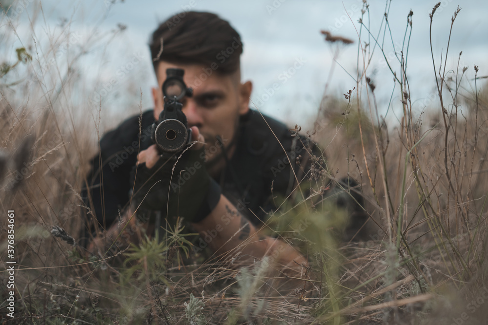 Young soldier in black uniform lying down and aiming an assault rifle ...