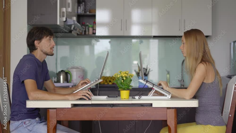 A young woman and man are working in their living room with the kitchen in the background. They both have to work remotely due to the Covid-19 restrictions. Covid-19 pandemics concept A young woman and man are working in their living room with the kitchen in the background. They both have to work remotely due to the Covid-19 restrictions. Covid-19 pandemics concept