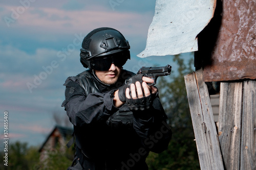 Special forces soldier in black uniform helmet and glasses aiming a pistol. © Nikita