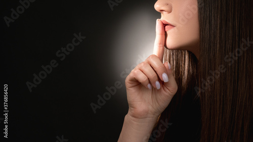 Stop talking. Domestic violence. Mysterious woman asking to keep quiet with finger on lips isolated on black empty space background. Betrayal gossip. Whistleblower secret. Social problem. photo