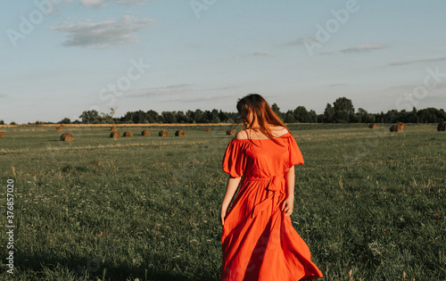 female model plus size in red dress on a field with haystacks, a beautiful young woman with brown hair, harvest concept