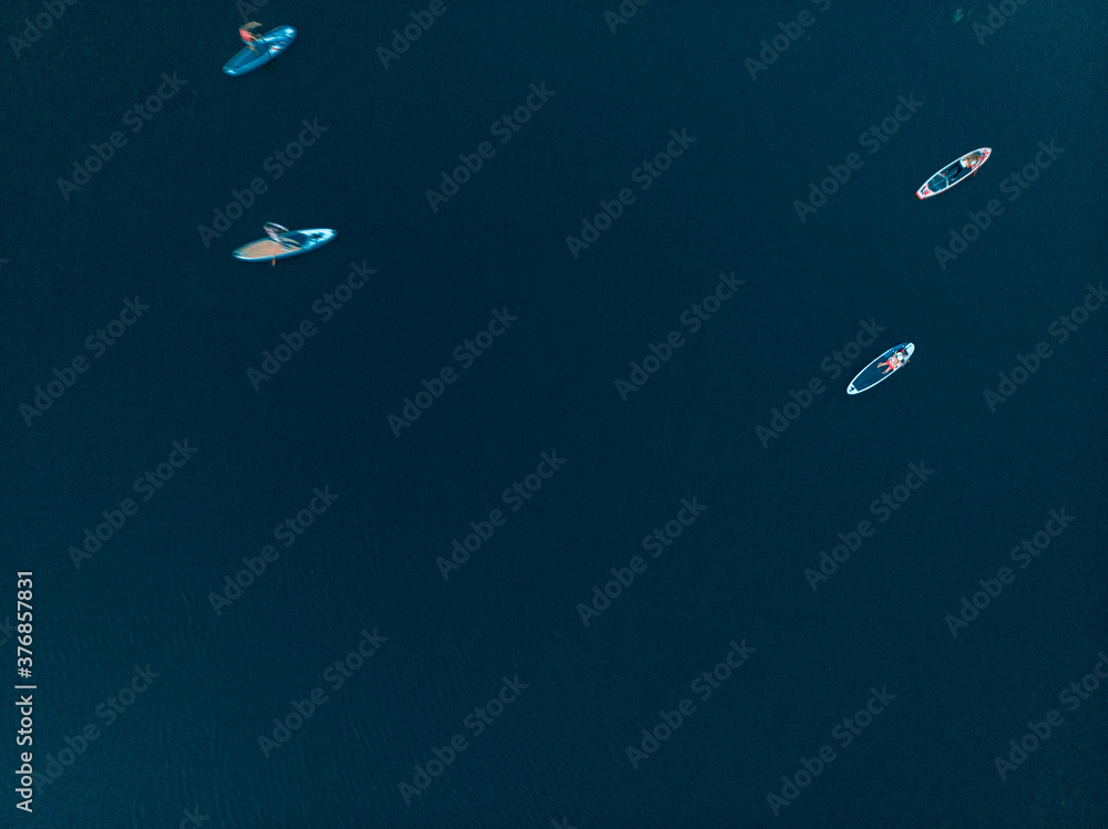 Top view of tourists on lake with SUP-boards. Beautiful clear water with people floating on boards engaged in sup-surfing. Seascape with people rowing on boards on background horizon Top view of tourists on lake with SUP-boards. Beautiful clear water with people floating on boards engaged in sup-surfing. Seascape with people rowing on boards on background horizon
