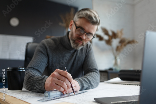 Interior designer working in office with blueprints.Engineer inspect architectural plan, sketching a construction project.Portrait of handsome bearded man at workplace. Business construction concept.