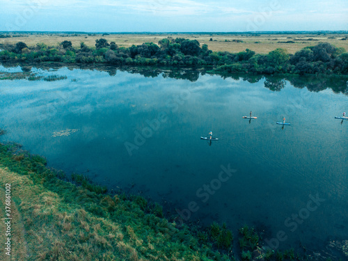 Top view of tourists on lake with SUP-boards. Beautiful clear water with people floating on boards engaged in sup-surfing. Seascape with people rowing on boards on background horizon