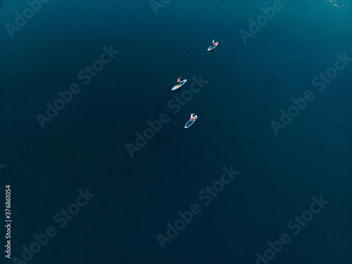 Top view of tourists on lake with SUP-boards. Beautiful clear water with people floating on boards engaged in sup-surfing. Seascape with people rowing on boards on background horizon