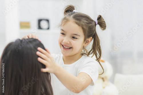 Close up photo of happy smiling schoolgirl touching her mother's hair.