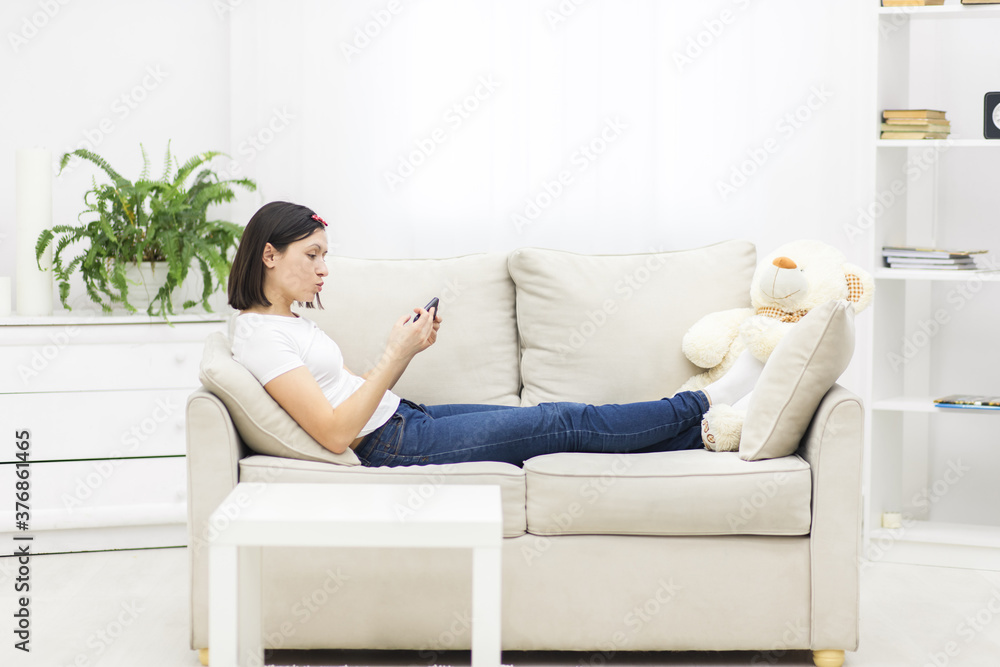 Photo of beautiful mother lying on sofa in living room and holding phone. Photo of beautiful mother lying on sofa in living room and holding phone.
