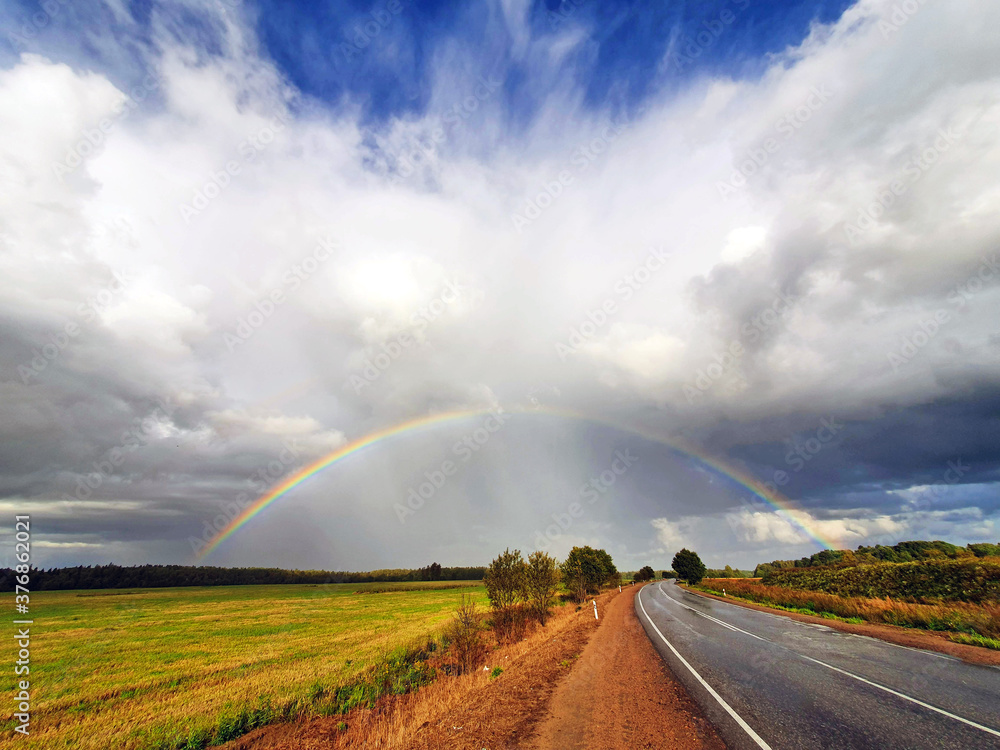 the phenomenon of a hemispherical rainbow in a natural landscape, fields, forests, road. the colorful spectacle of the appearance of a rainbow in late summer, autumn