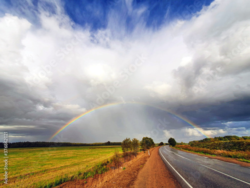 the phenomenon of a hemispherical rainbow in a natural landscape, fields, forests, road. the colorful spectacle of the appearance of a rainbow in late summer, autumn © Igor Pirozhkov