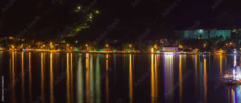 Beautiful Skyline Panorama Of Night City, lights reflecting over water, panorama. The town is called Eski Foca (in EN: Old Phokaia), located in Izmir, Turkey. Great reflections over sea.