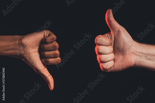 Like dislike gesture. Ethnic diversity. Closeup african male hand thumb down caucasian thumb up isolated on dark. Racial disagreement