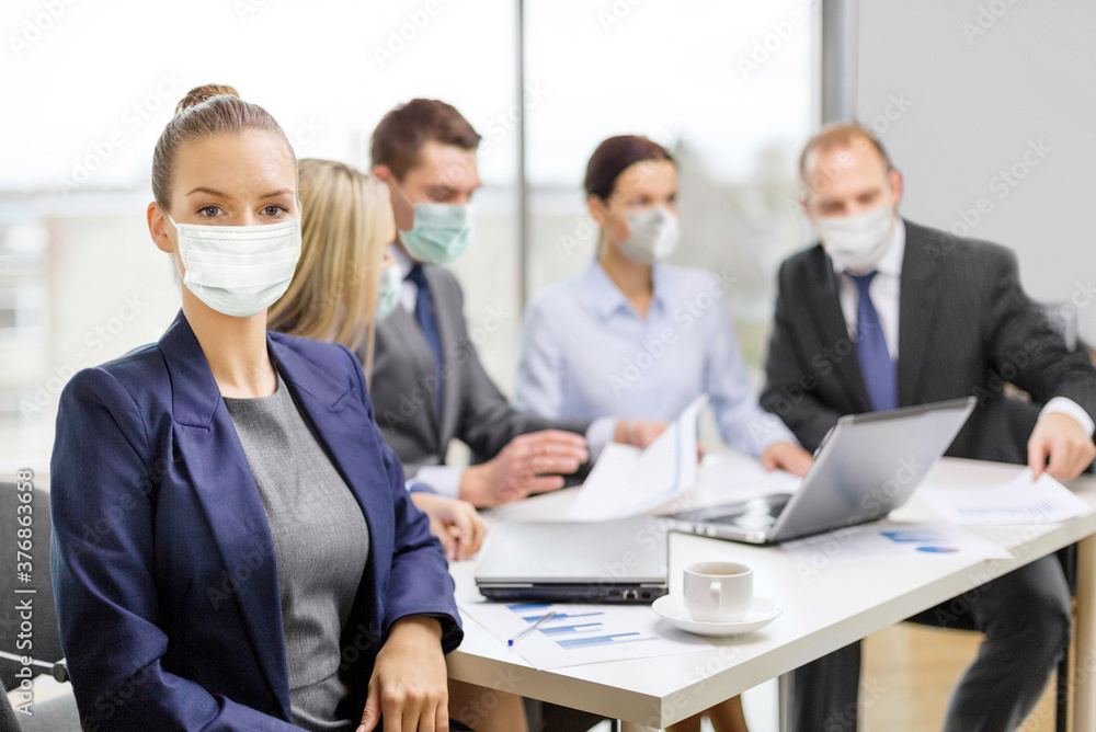 business and pandemic concept - businesswoman wearing face protective medical mask for protection from virus disease at office with team on the back business and pandemic concept - businesswoman wearing face protective medical mask for protection from virus disease at office with team on the back