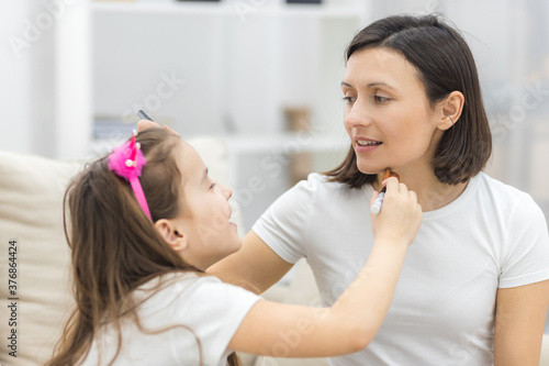 Pretty mother teaching her daughter doing make up at home.
