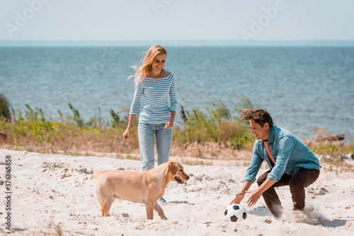 Couple with football and golden retriever playing on beach during weekend