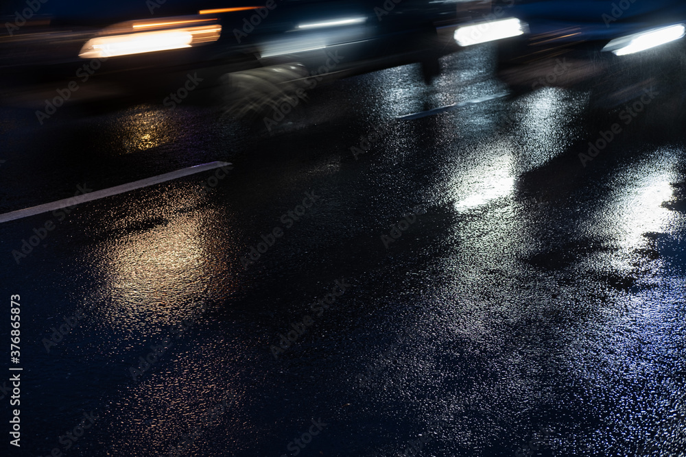 Night traffic of cars. Cars in motion on wet asphalt. Flickering headlights in the evening city.