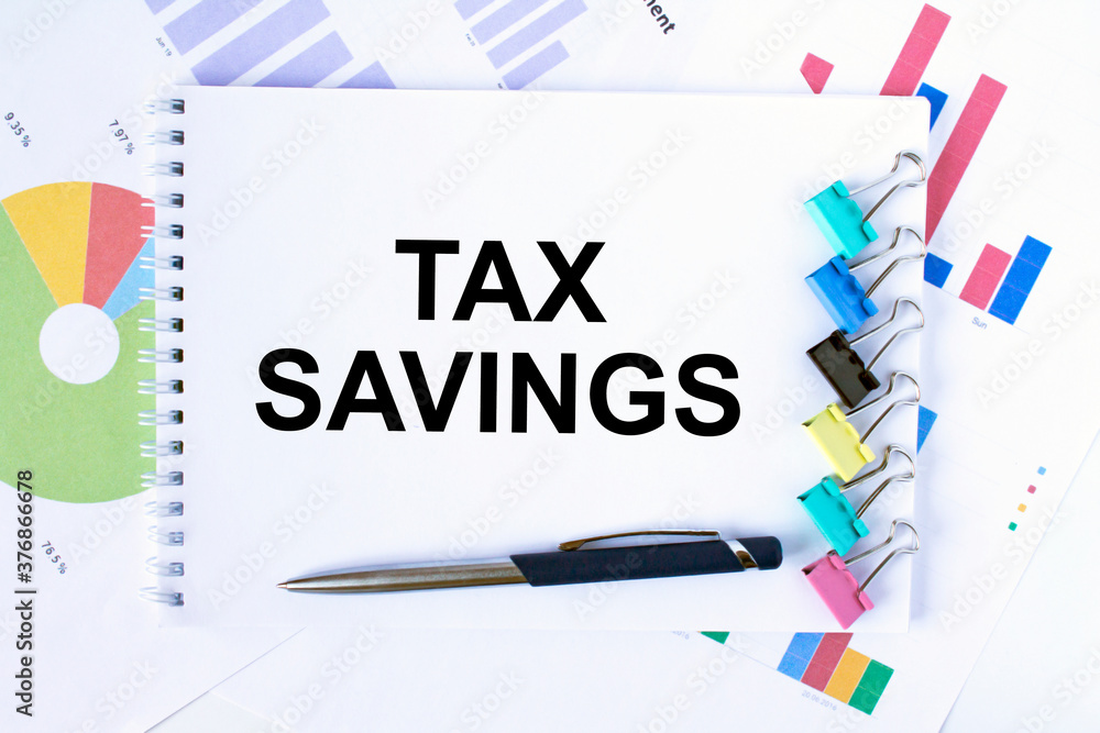 Notepad with text Tax Savings, paper clips, blue pen on financial diagrams Notepad with text Tax Savings, paper clips, blue pen on financial diagrams