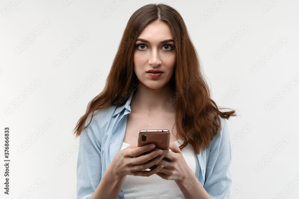 Young woman with long chestnut hair, using smartphone on white background. New useful application. Young woman with long chestnut hair, using smartphone on white background. New useful application.