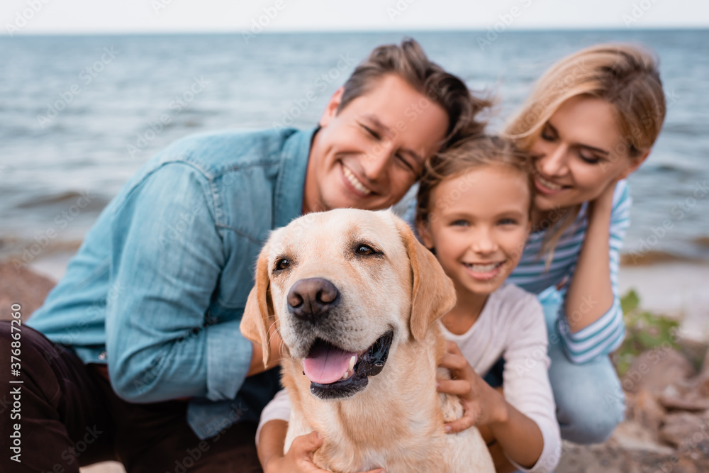 Selective focus of golden retriever sitting near family on beach Selective focus of golden retriever sitting near family on beach