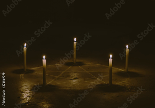 White pentagram symbol on concrete ground. Illuminated with candles. Dark background. Scary, mystical occultism 