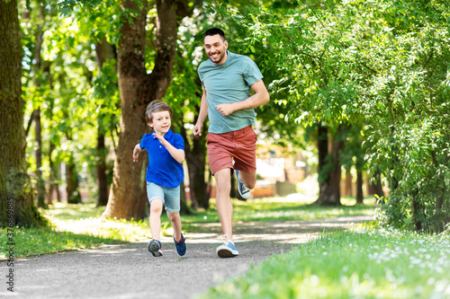 family, fatherhood and people concept - happy father with little son compete in running at summer park