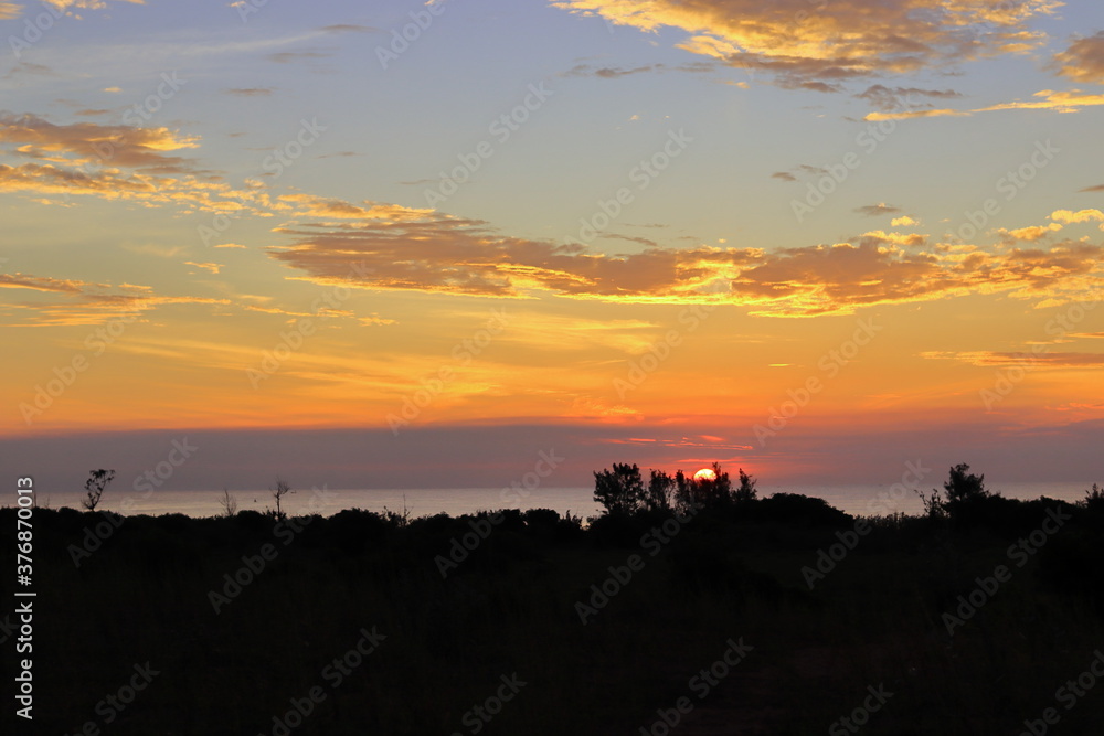 Photograph of a landscape with a view of the sun rising from the sea and clouds
