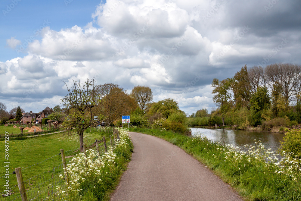 Rural road on a dike along the Linge river in springtime, with flowering cow parsley, in the background a small village