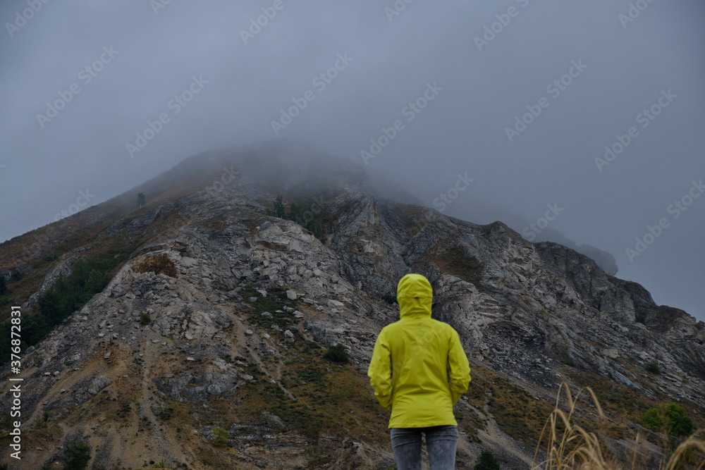 A young girl in a bright green jacket looks at a mountain in the fog.