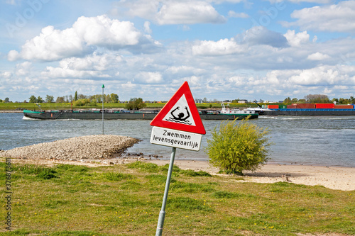 Odd road sign along the Waal river in Zaltbommel, Gelderland: dangerous swimming (in Dutch) and risk of drowning; a cargo ship passes by  photo