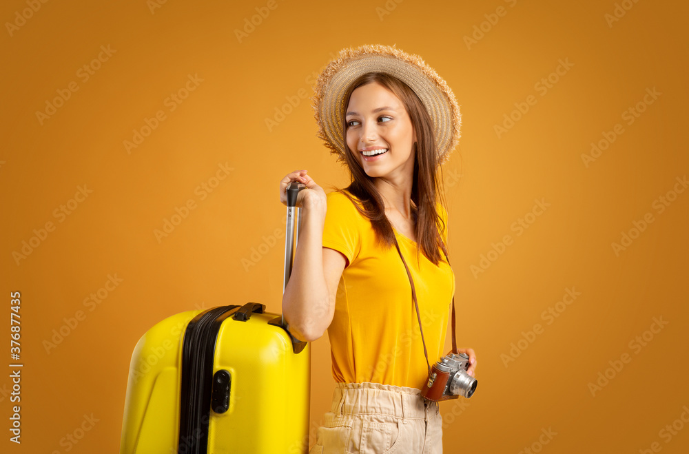 Smiling woman traveller with camera carrying suitcase