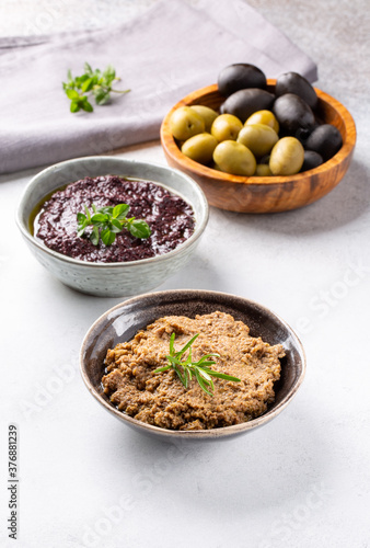 Tapenade - paste made from olives. Bowls with spreadable black and green olive cream on concrete background.
