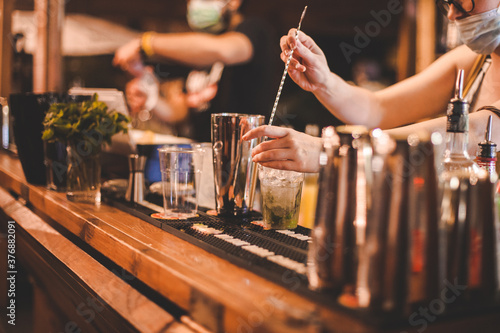 Dettaglio mani di baristi in un momento di preparazione di bevande alcoliche poste sopra di un bancone in legno in un locale estivo notturno photo