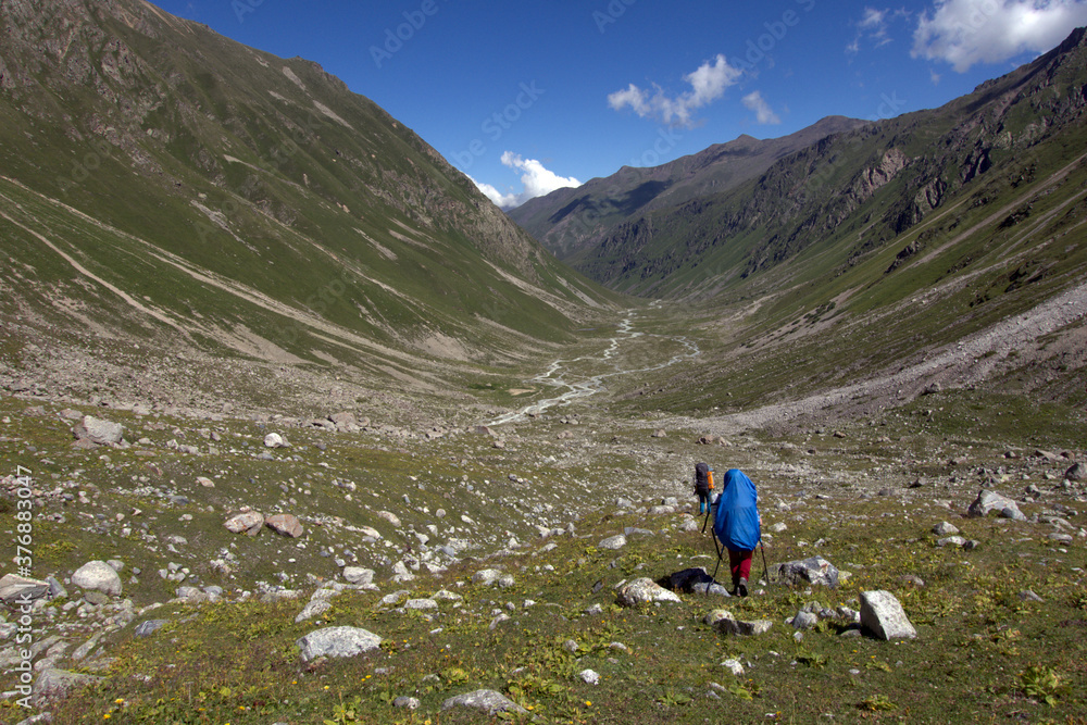 Backpackers trekking in mountains. Tourists with backpacks descend into the mountain valley. Caucasus.