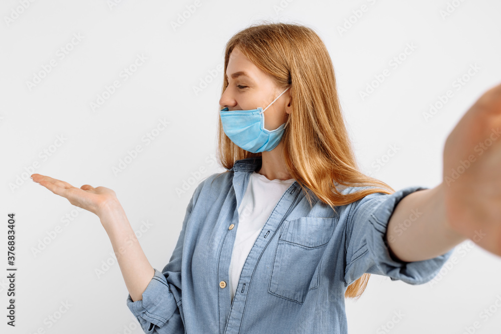 beautiful young woman in a medical protective mask on her face, points her finger at copyspace, white background beautiful young woman in a medical protective mask on her face, points her finger at copyspace, white background