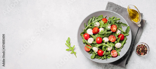 Diet and healthy salad with arugula, cherry tomatoes, mozzarella cheese and olive oil on white background. Top view, banner, copy space