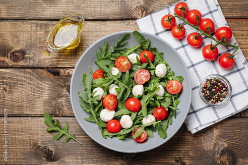 Diet and healthy salad with arugula, cherry tomatoes, mozzarella cheese and olive oil on wooden background