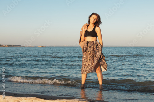 Atmospheric portrait of a young woman in  stylish skirt and coat walking on beach  in the background sea. The concept of female freedom and emancipation