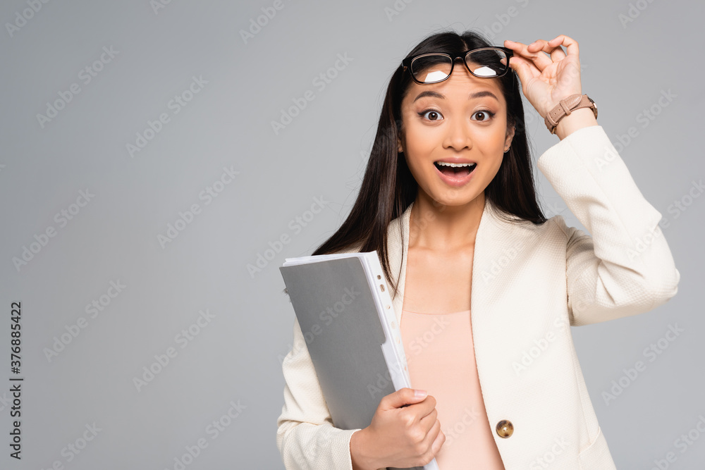 excited asian businesswoman touching eyeglasses while looking at camera with open mouth isolated on grey excited asian businesswoman touching eyeglasses while looking at camera with open mouth isolated on grey