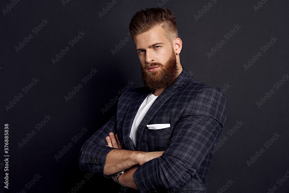 Handsome man keeping arms crossed and looking at camera while standing against grey background