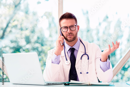 Male doctor using laptop and mobile phone while working in doctor's room