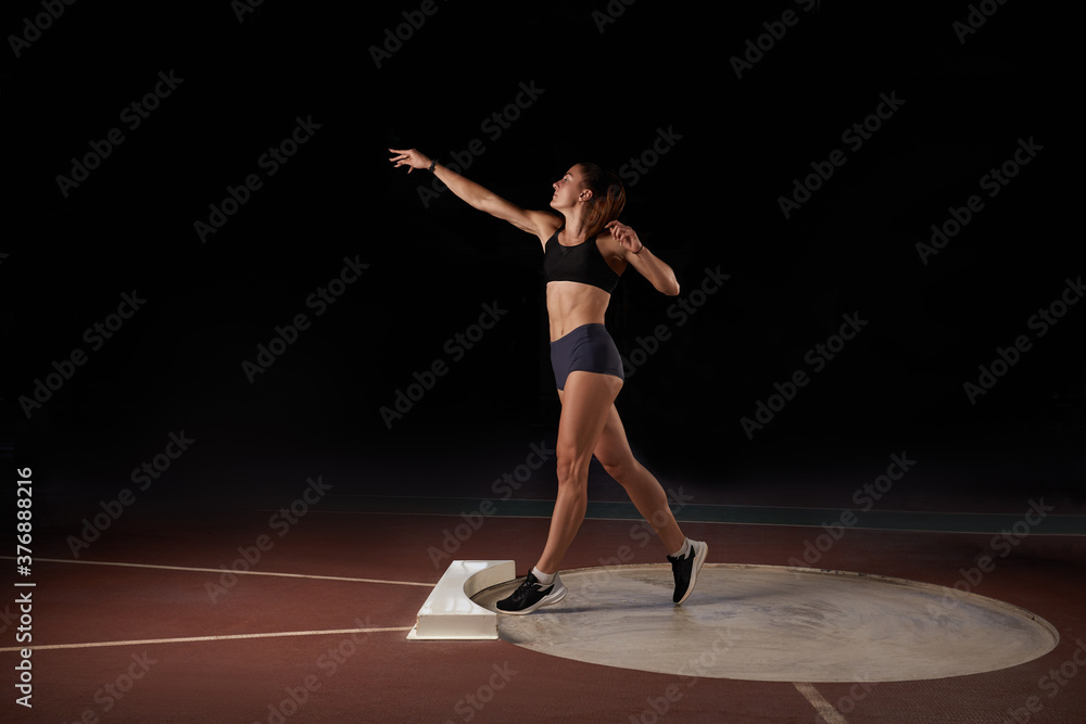 Female athlete doing a shot-put throw, black background