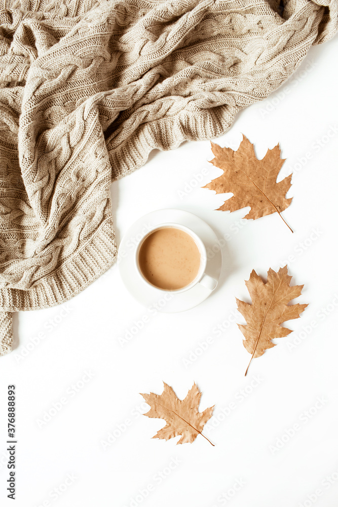 Cup of coffee with milk, beige knitted plaid, dry leaves on white background. Flat lay, top view.