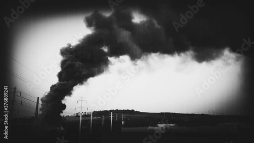 Dark smoke from burning building rising in to the sky. Old, vintage film look