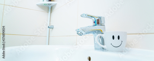 chromed metal faucet for hot and cold water   cup with smile face for toothbrushes  in a modern bathroom