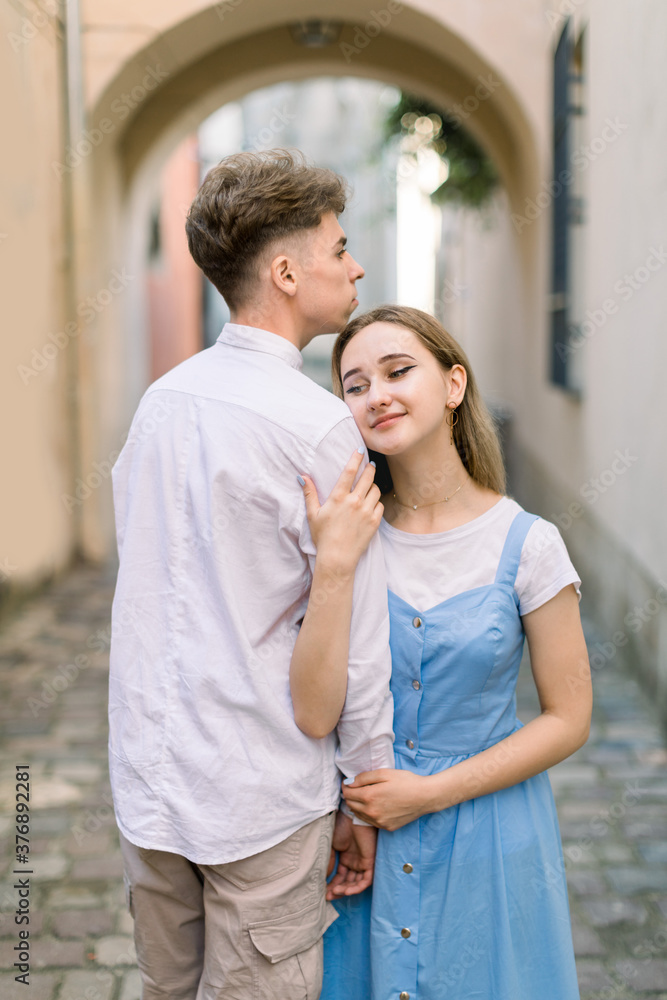 Romantic date outdoors in old European city. Portrait of stylish young couple in love, man in white shirt and girl in blue dress, posing to camera, while walking in the city. Romantic date outdoors in old European city. Portrait of stylish young couple in love, man in white shirt and girl in blue dress, posing to camera, while walking in the city.