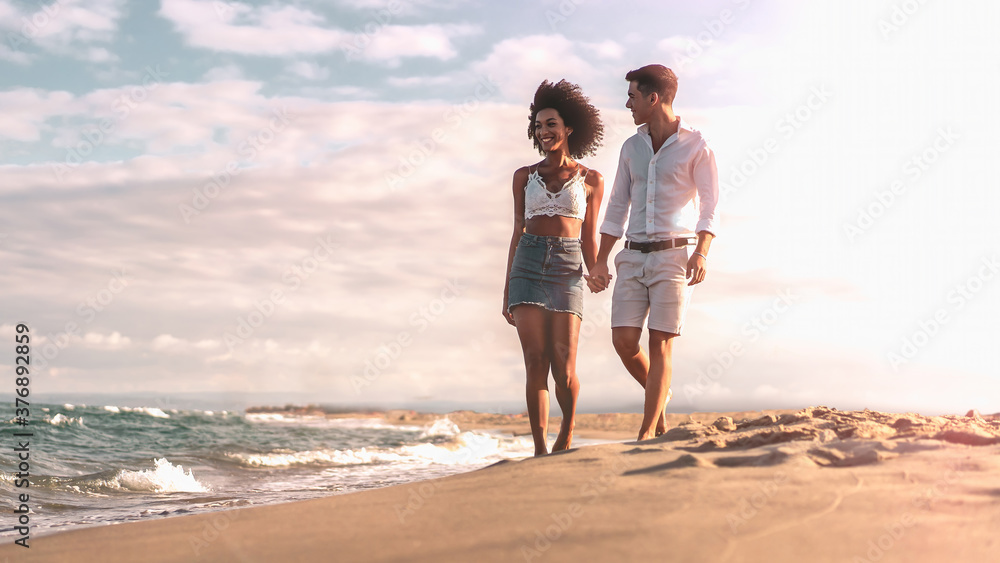 Multiethnic couple walking on the beach on the seashore in the evening. Romantic concept. Multiethnic couple walking on the beach on the seashore in the evening. Romantic concept.