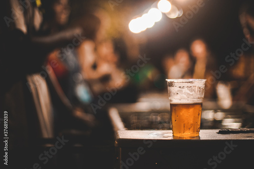 Primo piano immagine di bevanda alcolica poggiata vicino a dei ragazzi che giocano a calcio balilla all'aperto di notte photo